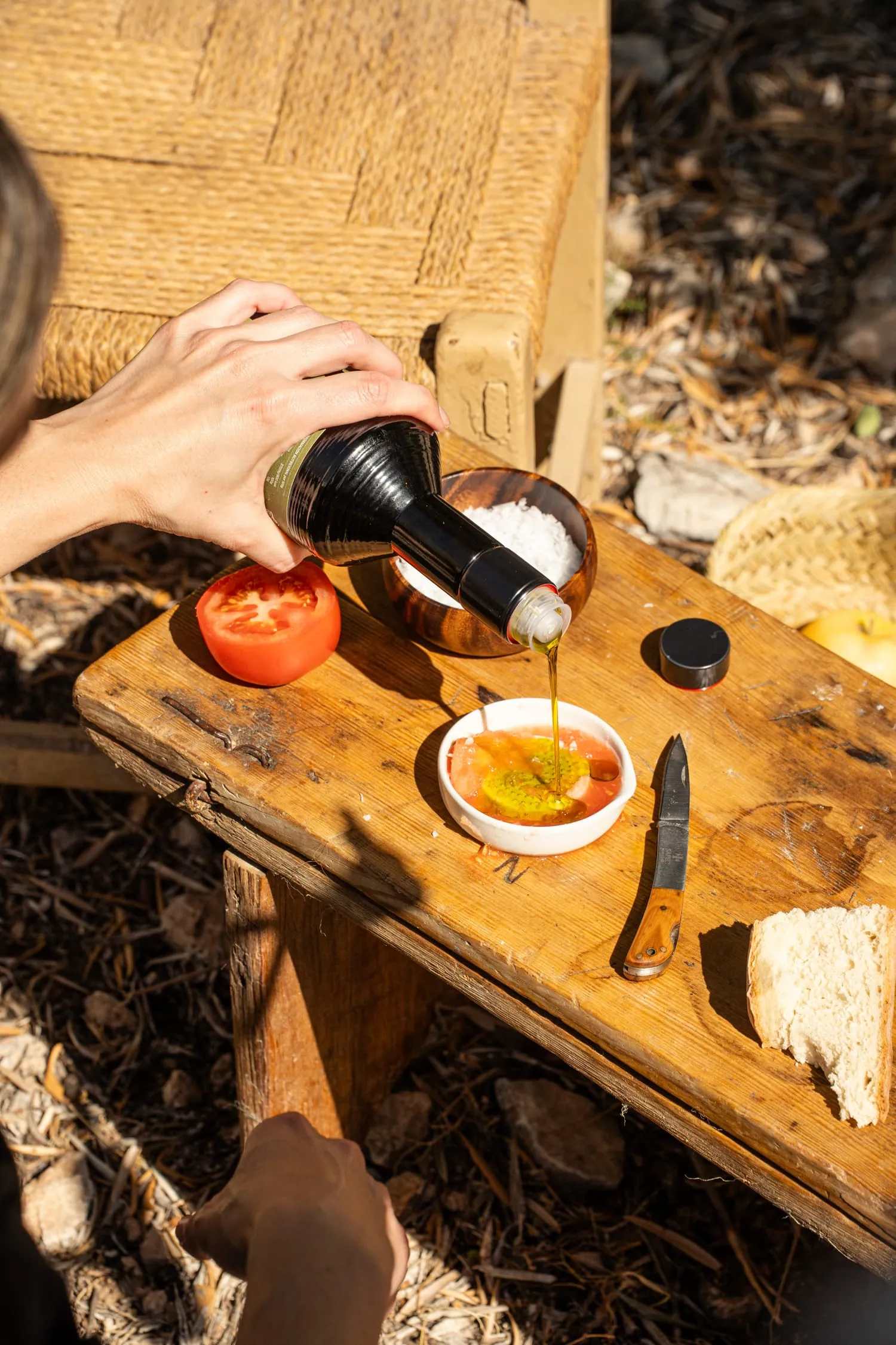 Aceite cayendo sobre tomate en un cuenco, en un banquito de madera, durante la merienda en la aceituna