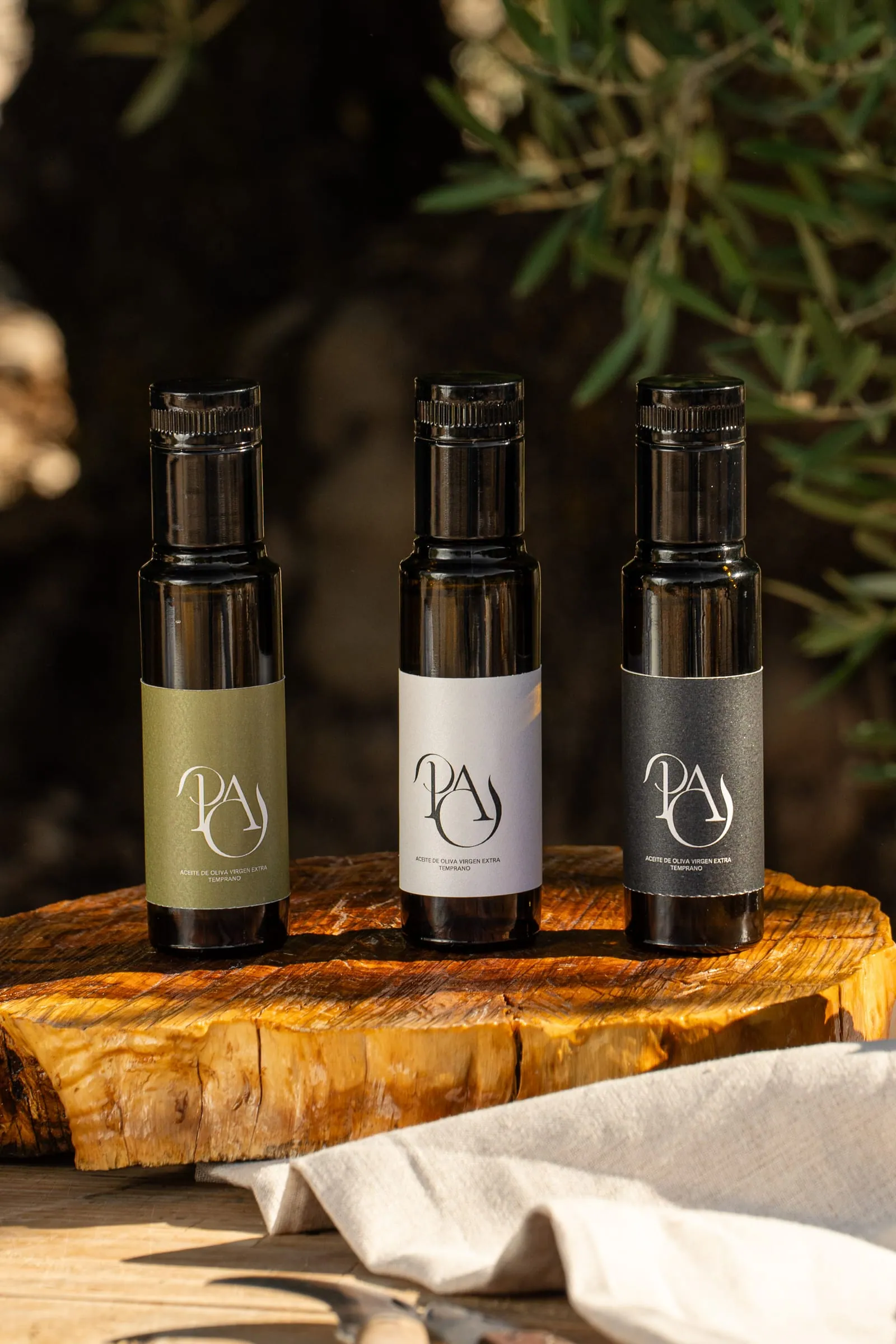 Tres botellas de 100 ml, una por cada aceite, sobre un tocón de olivo